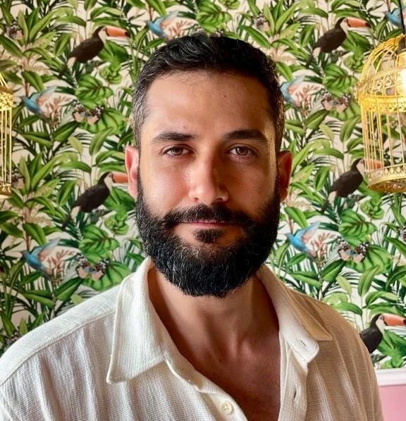 Mustapha Darbaj, in a cream open-collar shirt, against botanical wallpaper